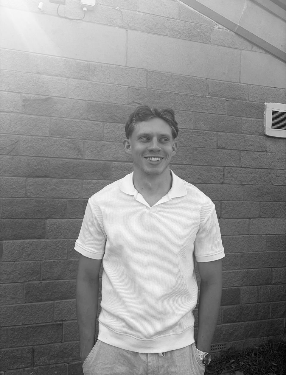 Elliott Harrison, smiling, standing against a stone wall